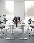 Lifestyle Office Image - Flokk HÅG Capisco chair showing contoured saddle seat and adjustable backrest, seats shown with and without neck/head supports being used at a sit stand desk setup.