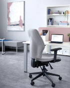 Orthopaedica 200 series task chair by Torasen. The chair is in an office and fully upholstered in grey fabric with black components including black adjustable arms, mechanism levers and 5 star castor base.
