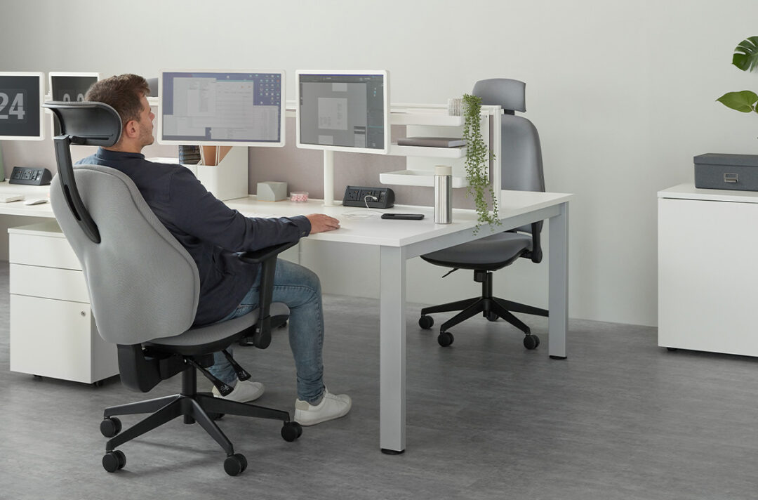 Ergonomic Task Chair with a Built In Headrest in an office workstation set-up. The chair is fully upholstered in a grey fabric with black accessories including arms and 5 star castor base. Torasen 100 Series Range